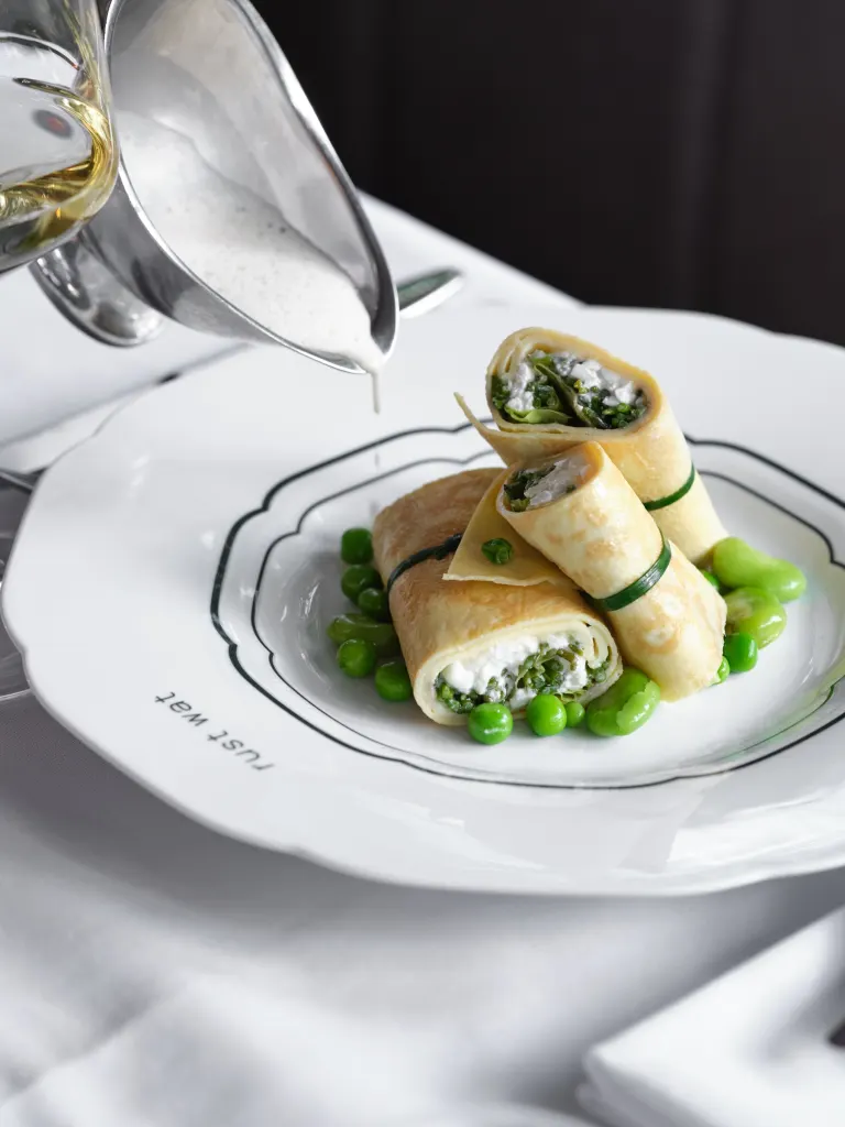Gevulde crêpes met doperwten, saus wordt aan tafel geschonken